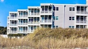 A beachfront hotel with multiple balconies, a sandy beach in the foreground, and a clear blue sky. - OCEANFRONT -  “Little piece of paradise” @ 206 Windsong in Windy Hill, N. Myrtle (North Myrtle Beach)