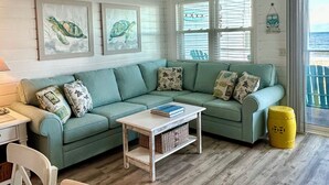A living room with a green sofa, a white coffee table, and a ceiling fan. - OCEANFRONT -  “Little piece of paradise” @ 206 Windsong in Windy Hill, N. Myrtle (North Myrtle Beach)