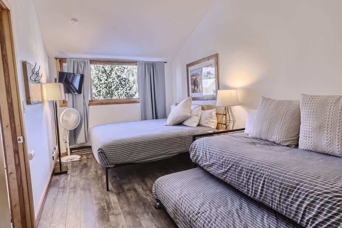 Ein kleines, gemütliches Zimmer mit zwei Einzelbetten, einem Fernseher, einem Ventilator und einem Fenster mit Vorhängen.