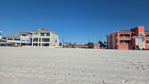 Ein Strandgrundstück mit großem Sandbereich, einem mehrstöckigen Gebäude mit Balkonen und einem kleineren Anbau.
