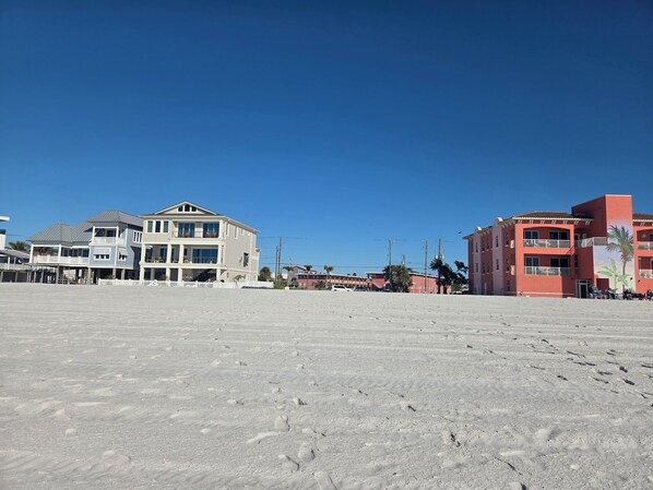 A beachfront property with a large sandy area, a multi-story building with balconies, and a smaller adjacent structure.