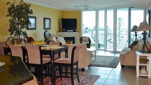 A living room with a dining area, a fireplace, and a large window with a view. - Relax & Enjoy - Coastal Paradise!  SUNDAY- SUNDAY RENTAL ONLY DURING PEAK SEASON (Orange Beach)