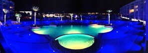 Ein Poolbereich bei Nacht mit beleuchteten Wasserspielen und Sitzbereichen.