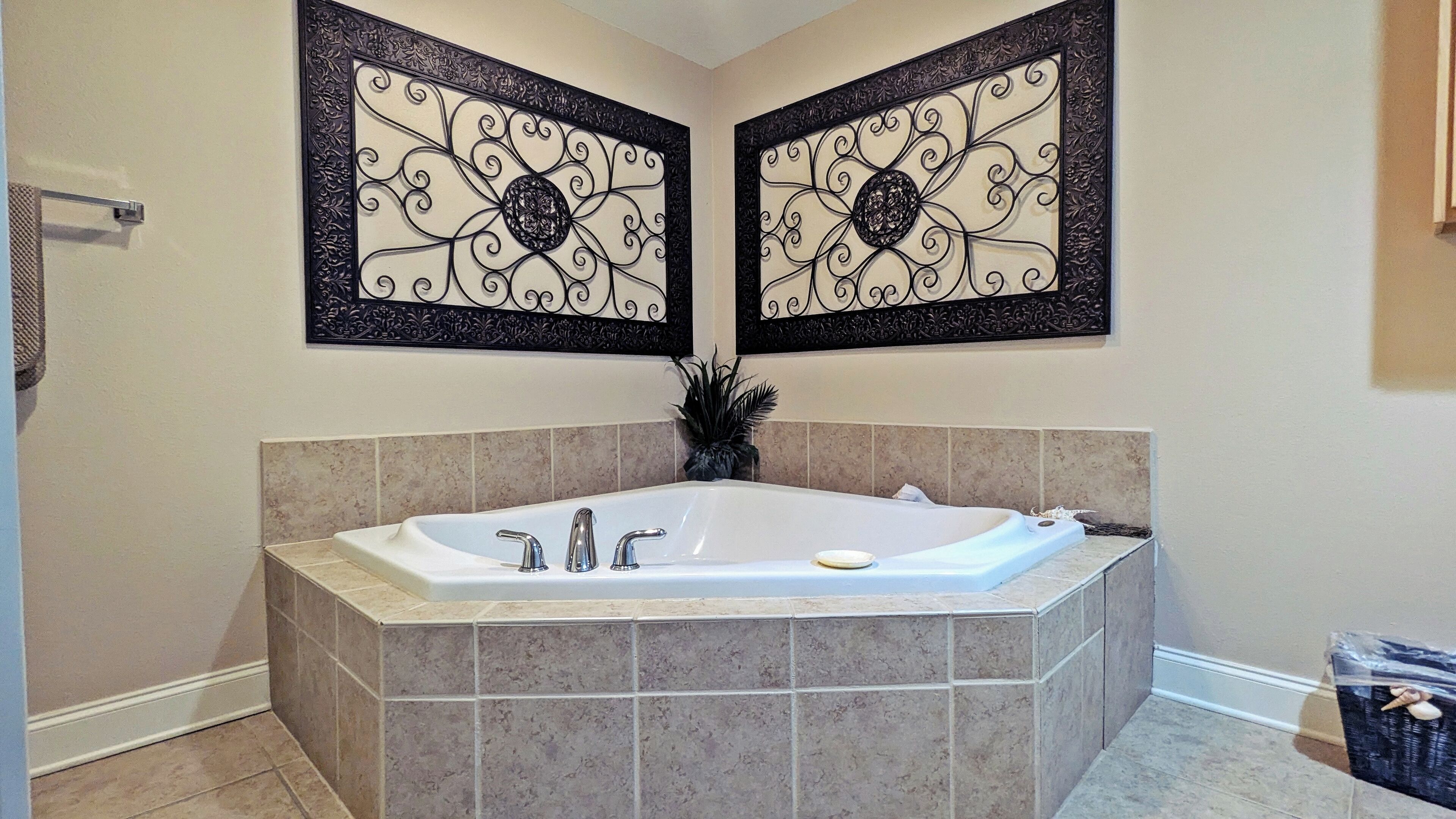 Une salle de bain avec une baignoire sur pieds, deux panneaux décoratifs fixés au mur et une plante en pot.