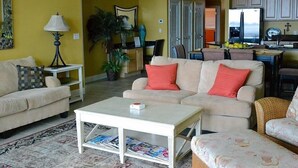 A living room with a sofa, coffee table, and a dining area with chairs and a table. - Relax & Enjoy - Coastal Paradise!  SUNDAY- SUNDAY RENTAL ONLY DURING PEAK SEASON (Orange Beach)