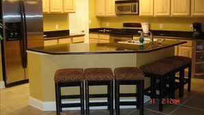 A kitchen with a central island, a refrigerator, a microwave, and a coffee maker. There are three stools at the island. - Relax & Enjoy - Coastal Paradise!  SUNDAY- SUNDAY RENTAL ONLY DURING PEAK SEASON (Orange Beach)