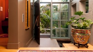 A hallway with a sliding glass door leading to a garden area, a large decorative pot with plants, and a framed artwork on the wall. - LARGE CONTEMPORARY HOME ON THE SAND, HOT TUB, CHEF’S KITCHEN, ENDLESS VIEWS (Capistrano Beach)