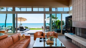 A modern living room with a glass wall overlooking the ocean, leather furniture, and a fireplace. - LARGE CONTEMPORARY HOME ON THE SAND, HOT TUB, CHEF’S KITCHEN, ENDLESS VIEWS (Capistrano Beach)