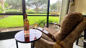 A room with a large window, a patterned sofa, a small round table, and a bottle of wine.