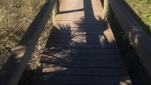 A wooden boardwalk leading to a beach with blue umbrellas and chairs.