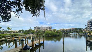 A calm water body with wooden docks and a reflection of the sky. In the background, there are multi-story buildings with a modern design.