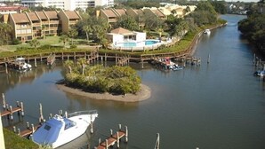 A marina with boats docked, a small island with a pool, and buildings in the background.