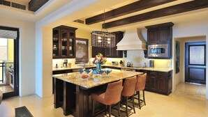A modern kitchen with dark wood cabinets, a large island with bar stools, and a stainless steel microwave. - 3rd Night Free-Luxury Oceanview HBC Resort Residence-Medano Beach (Cabo San Lucas)