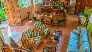Un amplio salón con mesa de comedor, mobiliario de mimbre y una cocina al fondo.