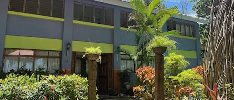 A building with a two-story structure, large windows, and a garden area with potted plants and a pathway.