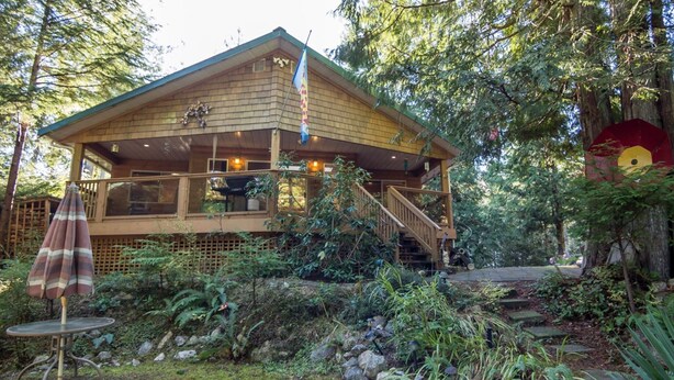 Eine Holzhütte mit einer Veranda, umgeben von üppiger Vegetation und einem Steinweg.
