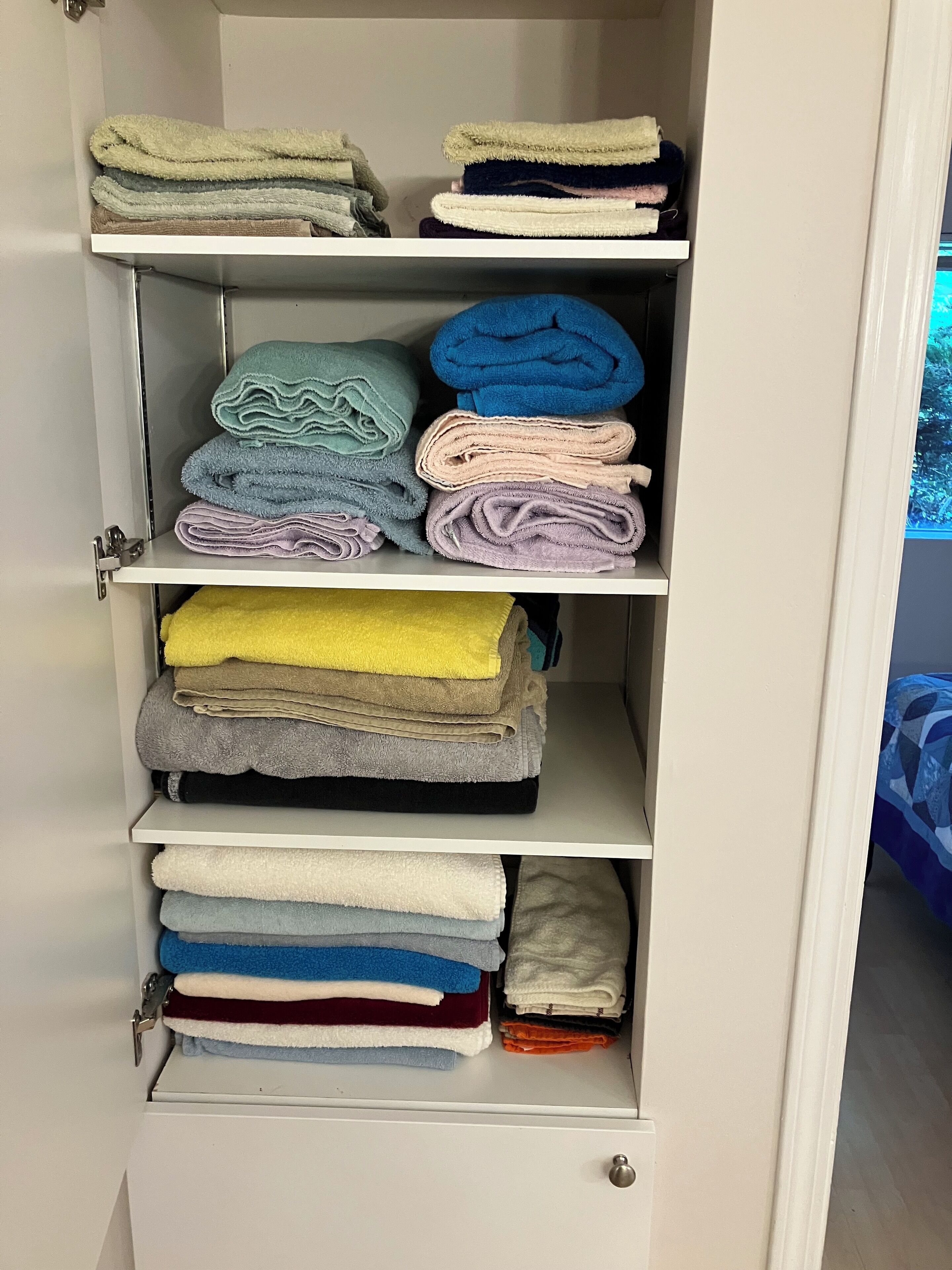 A wardrobe with multiple shelves holding folded towels in various colors.