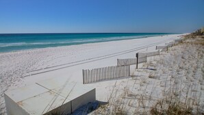 En strand med hvidt sand, et træhegn og en klar, blå himmel.