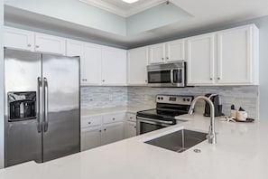 Uma cozinha moderna com armários brancos, eletrodomésticos de aço inoxidável, uma pia dupla e painel de azulejos.