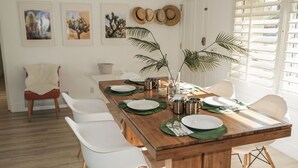 A dining area with a wooden table set for six, white chairs, and a plant in the center.