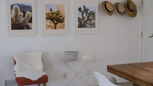 A room with a wooden dining table, a white chair, a red chair with a white throw, and three framed desert landscape pictures on the wall.
