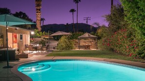 A swimming pool with a curved edge, surrounded by a patio area with outdoor furniture and a covered seating area.