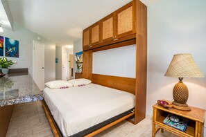 A neatly made bed with a wooden headboard, a small bedside table with a lamp, and a magazine rack. - 15% OFF SEPT & OCT 7nt stays Remodeled Kihei Oceanfront Property, AC, Pool & BBQ (Kihei)