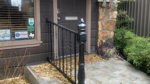 Une maison avec une porte brun foncé, un petit porche doté d’une balustrade noire et un escalier en pierre menant à la porte.