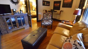 Un salon comprenant un canapé en cuir, un fauteuil à motifs, un meuble en bois, un téléviseur et une table avec une lampe.