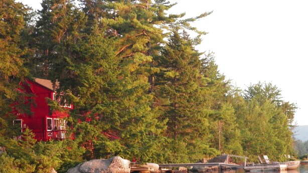 Een rood gebouw omringd door dichte bomen en een rustig meer met boten.