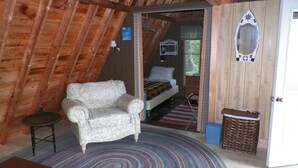 Een knus ingerichte kamer met een gestreept fauteuil, een bed met een kleurrijk plaid en een klein rieten mandje.