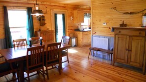 A wooden cabin interior with a dining area, kitchen, and a large window. - Woodland secluded cabin on 7 acres, with private dock and kayaks (Leitchfield)
