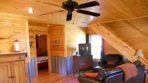 A cozy cabin interior with a wooden ceiling, a ceiling fan, a television, a leather sofa, and a dining area with a wooden table and chairs. - Woodland secluded cabin on 7 acres, with private dock and kayaks (Leitchfield)
