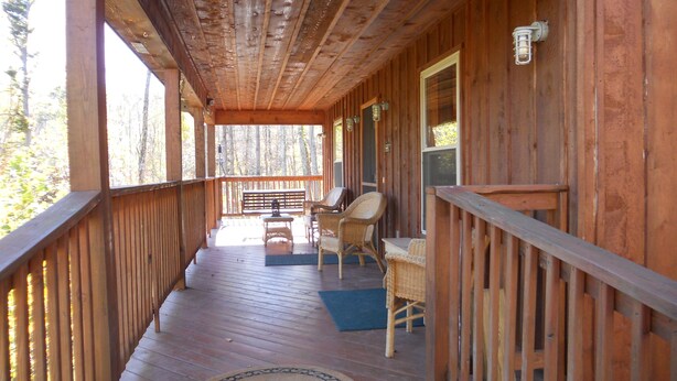 A wooden porch with a bench and chairs, a doormat, and a view of the forest. - Woodland secluded cabin on 7 acres, with private dock and kayaks (Leitchfield)
