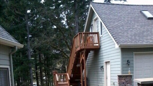 A house with a wooden deck, a stone fireplace, and a staircase leading to a deck area.