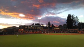 Un campo de béisbol con un estadio al fondo durante el atardecer.