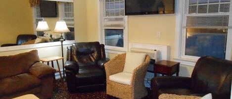 A living room with a sofa, armchair, and a TV mounted on the wall.
