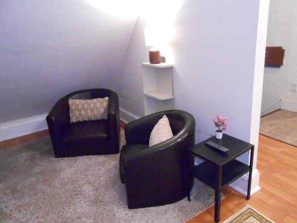 Una habitación con dos sillones negros, una pequeña mesa con un florero y un estante blanco contra una pared morada.