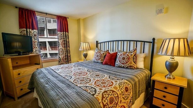 Un dormitorio con una cama, dos mesitas de noche, un televisor y una ventana con cortinas.