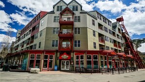 A multi-story hotel with a red and beige facade, featuring balconies and a prominent red staircase. - Outstanding 2BR in River Run. Fully stocked, steps from gondola and shopping (Dillon)