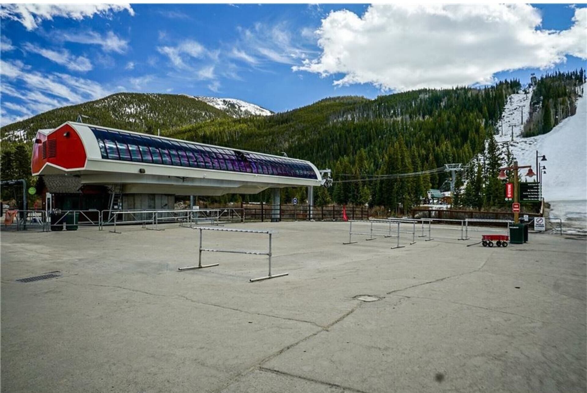 A large, modern building with a distinctive red and white color scheme, situated in a mountainous area with a clear sky and snow-capped peaks in the background.