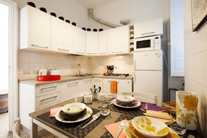 A modern kitchen with white cabinets, a microwave, and a refrigerator. There is a dining table with plates, cups, and a cake.