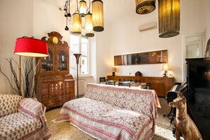 A cozy living room with a patterned sofa, a red lamp, a wooden cabinet, a piano, and a dog statue.