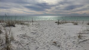 Une plage de sable avec une végétation clairsemée et une mer calme sous un ciel nuageux.