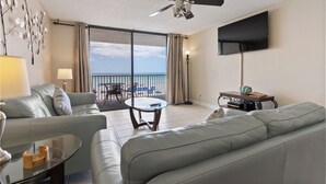 Ett hotellrum med en takfläkt, en platt-TV, en soffa, ett soffbord och utsikt över havet.