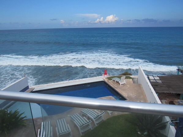 A pool with a view of the ocean and waves crashing onto the shore.