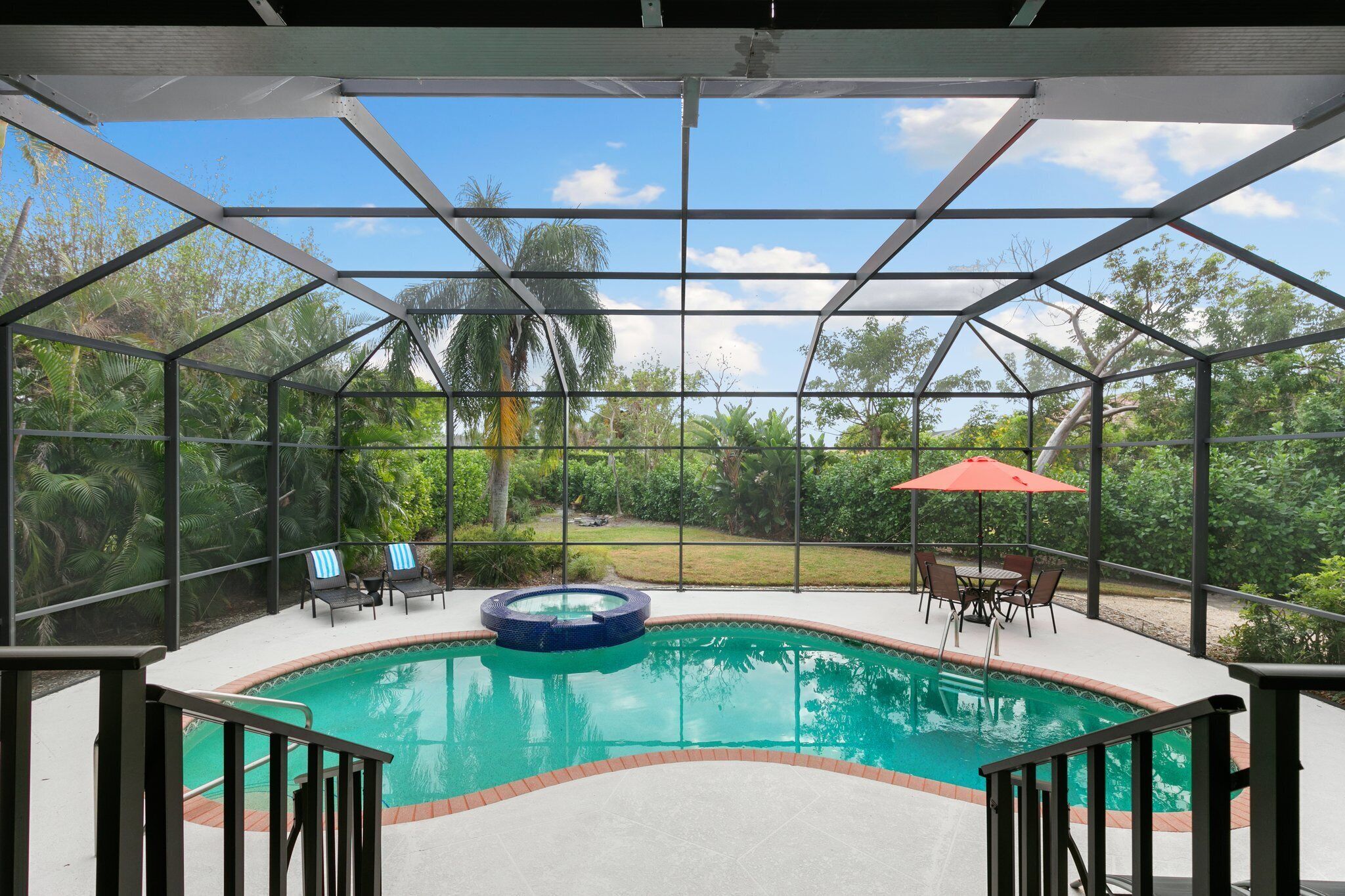 Un área de piscina con cerramiento de vidrio, un jacuzzi y mobiliario exterior.
