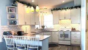 A kitchen with white cabinets, a central island with bar stools, a stove, and pendant lighting.