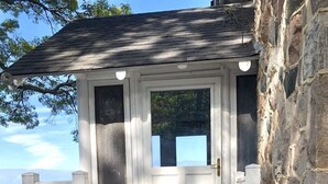 A stone house with a white front door, a small porch with steps, and a view of the sky and trees.