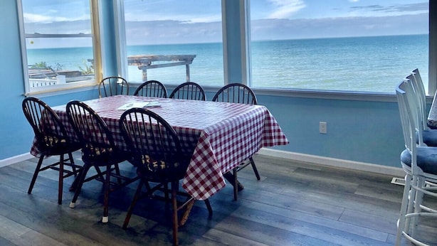 A dining area with a table set for six, large windows offering a view of the sea, and a blue wall.